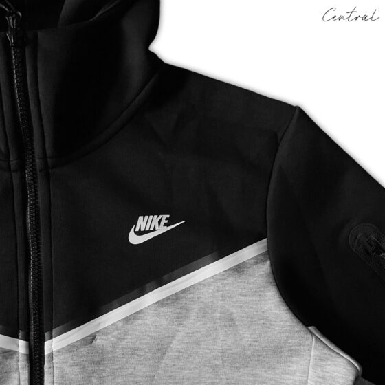 Nike Tech Fleece tracksuit in grey and black featuring a hoodie and matching pants set laid out flat.