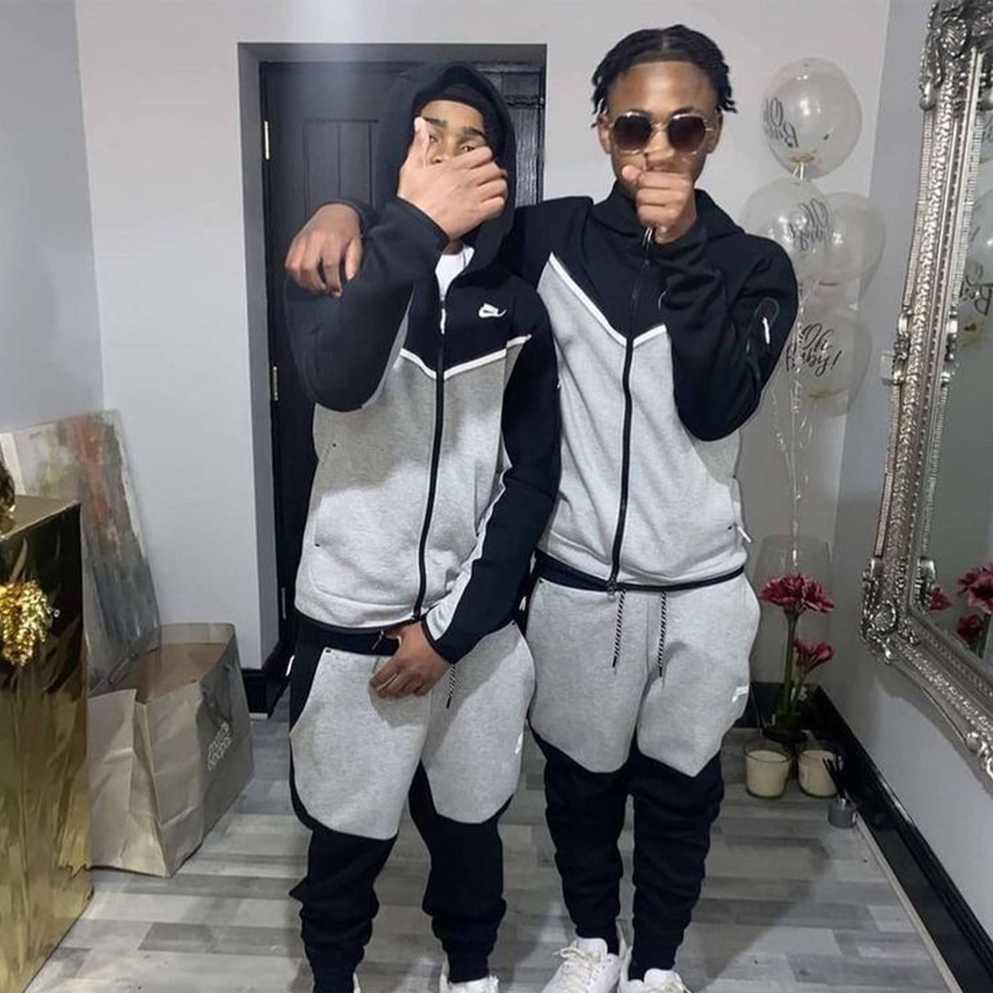Nike Tech Fleece tracksuit in grey and black featuring a hoodie and pants set, displayed on a neutral background.