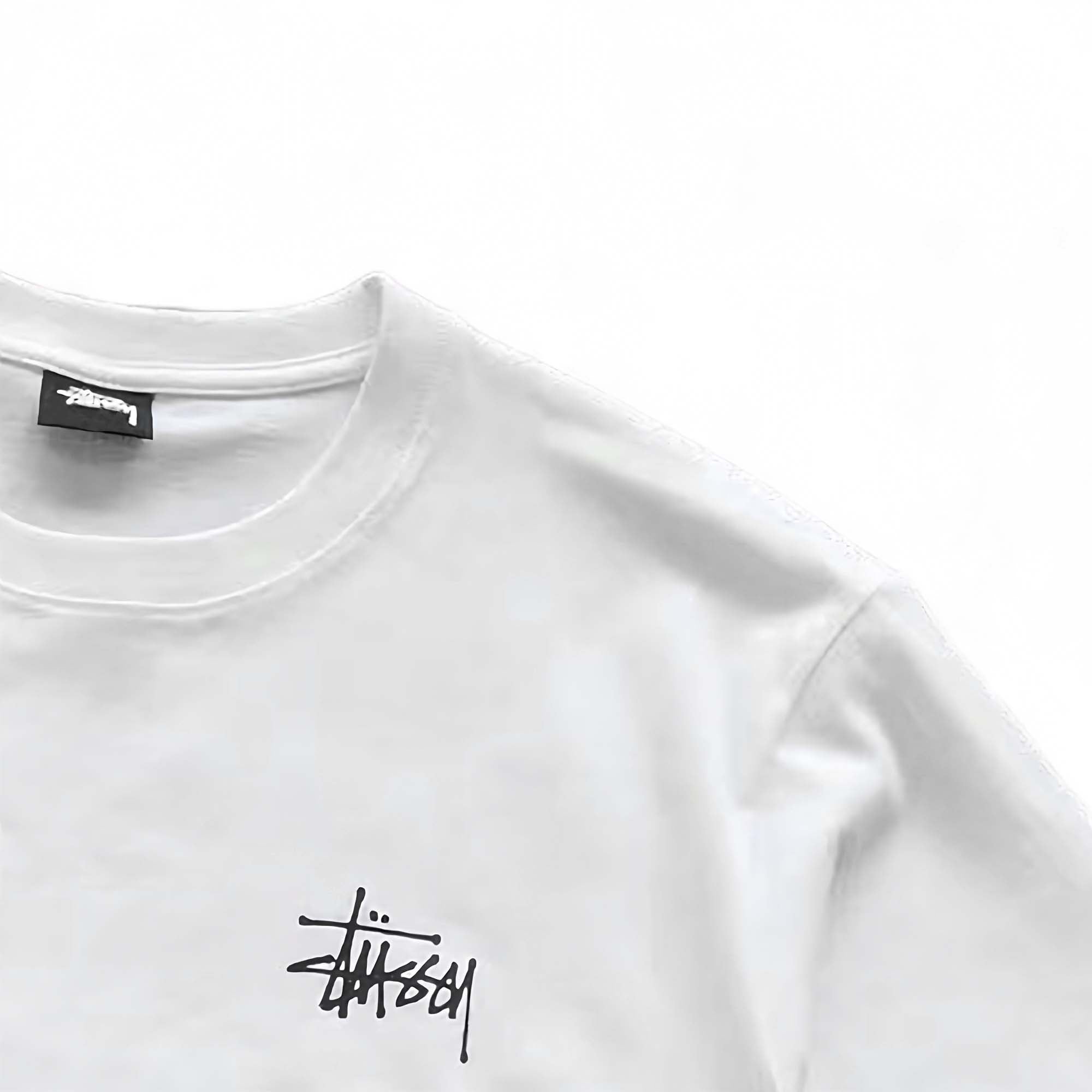 White BASIC STÜSSY TEE featuring a relaxed fit and logo detail, displayed on a plain background.
