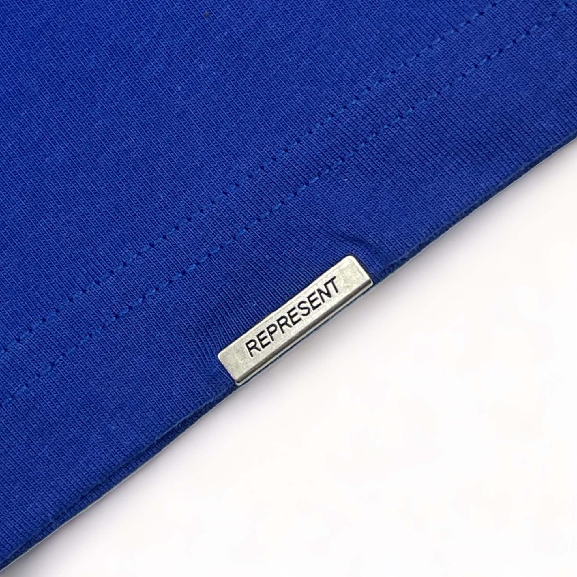 Cobalt blue REPRESENT OWNERS CLUB T-shirt displayed on a flat surface, showcasing front design and fabric texture.